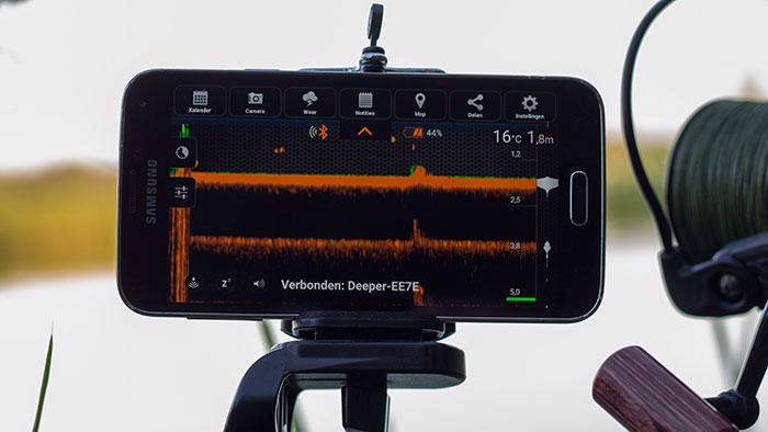 De Smartphone bevestigd op een klem van ene selfie stick (de meeste selfie sticks hebben namelijk schroefdraad voor een statief  ;-)